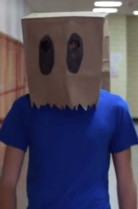 [Image: confidential-looking surveillance photograph or silhouette of Bag Man wearing a paper bag mask]